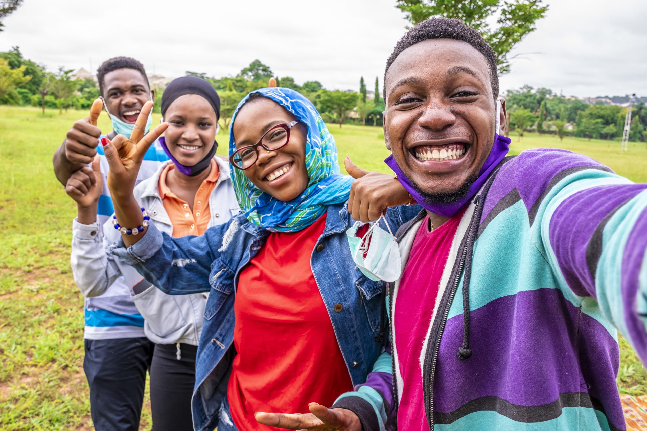 Group of cheerful African friends with facemasks taking a selfie in a park
